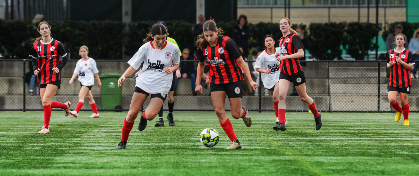 Soccer game in progress with players on a field, one player kicking the ball.