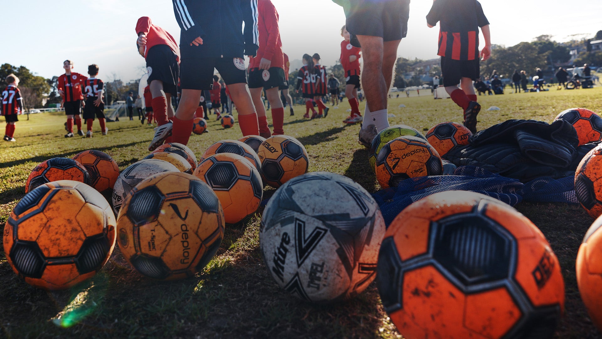Multiple soccer balls on the grass with players in the background